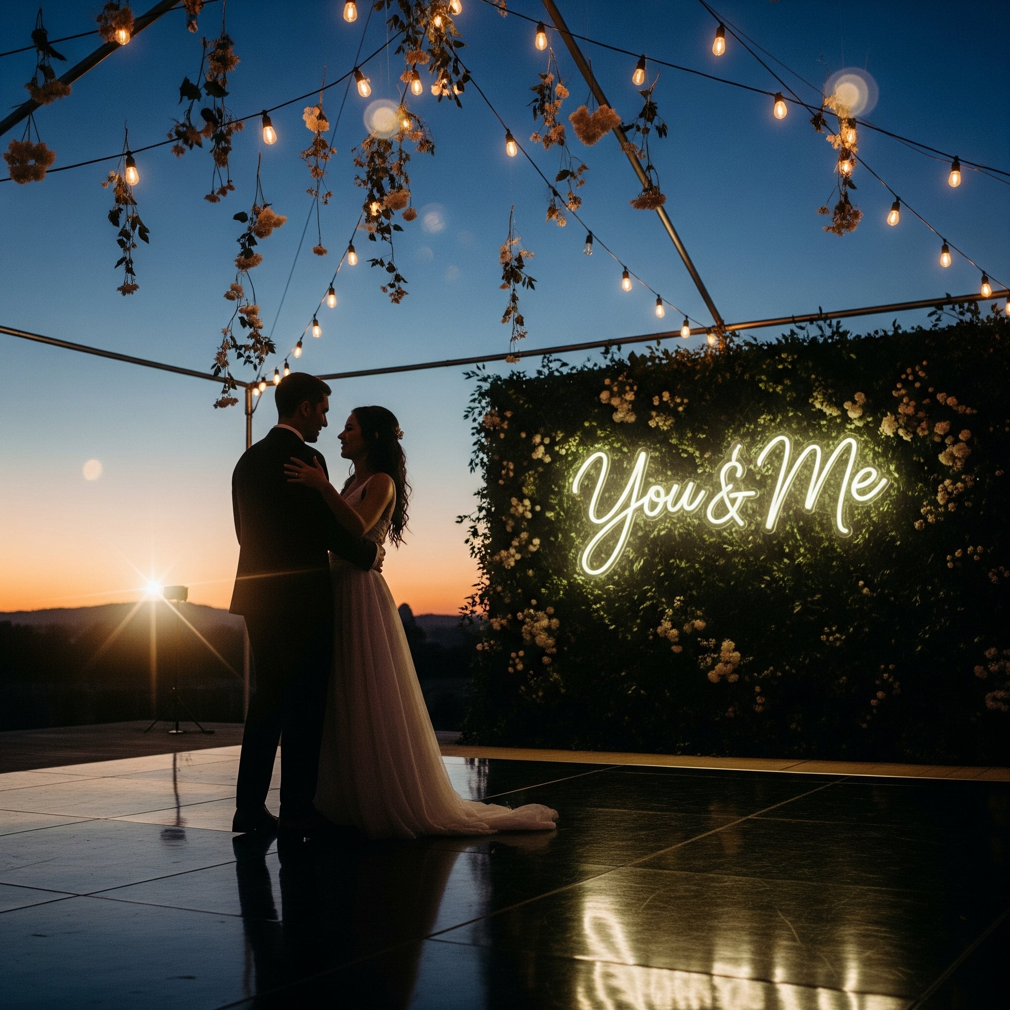 Bride and groom dancing under string lights with 'You & Me' neon sign at sunset